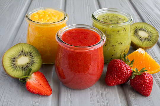 Different fruit smoothie or puree in the small glass jars on the gray  wooden background. Close-up.
