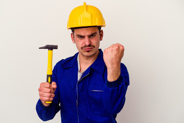 Young caucasian worker man holding a hammer isolated on white background showing fist to camera, aggressive facial expression.