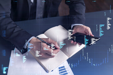 A trader in formal wear writing down some quotes to research stock market trends using smart phone for right investment solutions. Wealth management concept. Hologram Forex chart over close up shot.
