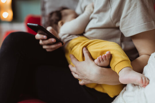Midsection of mother with baby boy using smart phone in living room