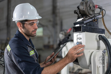 Male automation engineer checking and inspection control a robot arm welding .machine with tablet...