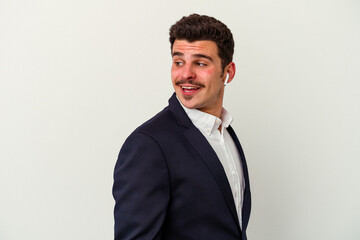 Young business caucasian man wearing wireless headphones isolated on white background looks aside smiling, cheerful and pleasant.