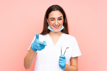 Woman dentist holding tools isolated on pink background points finger at you