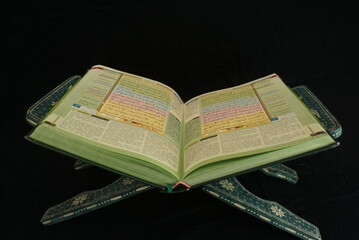 Photo of an open Islamic holy book against a black background and incoming light. suitable as a...