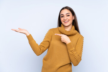 Young caucasian woman isolated on blue background holding copyspace imaginary on the palm to insert...