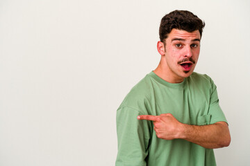 Obraz premium Young caucasian man isolated on white background smiling and pointing aside, showing something at blank space.