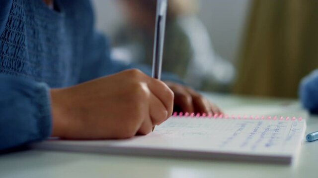 Girl writing in notebook at desk in classroom. Student doing classwork at school