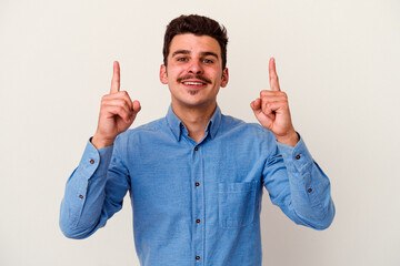 Young caucasian man isolated on white background indicates with both fore fingers up showing a...
