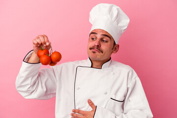 Young caucasian chef man holding tomatoes isolated on pink background