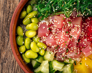 Hawaiian tuna poke bowl with vegetables on wooden background