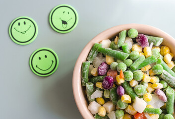 Frozen vegetables on a colored background top view. The concept of food in a pandemic frozen vegetables and positive emoticons close up