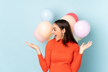 Young woman with many balloons isolated on blue background