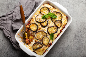 Greek mediterranean dish Moussaka with baked eggplants, ground beef in white ceramic casserole on rustic stone background from above, traditional dish of Greece