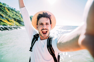 Happy young tourist taking selfie at beach on vacation - Millennial guy having fun smiling at...