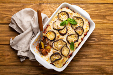 Greek mediterranean dish Moussaka with baked eggplants, ground beef in white ceramic casserole with napkin on wooden rustic background from above, traditional dish of Greece