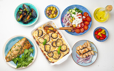 Assorted Greek dishes on white stone background from above, moussaka, grilled fish, souvlaki, greek salad, steamed mussels with herbs, appetizers of Greece from above 