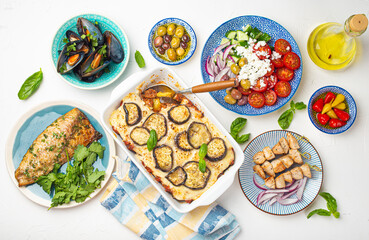 Assorted Greek dishes on white stone background from above, moussaka, grilled fish, souvlaki, greek salad, steamed mussels with herbs, appetizers of Greece from above 