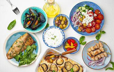 Assorted Greek dishes on white stone background from above, moussaka, grilled fish, souvlaki, greek salad, steamed mussels with herbs, appetizers of Greece from above 