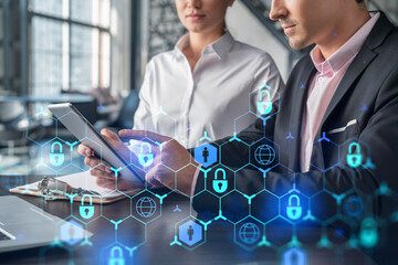 Businessman and businesswoman working together to protect clients confidential information and cyber security. IT hologram padlock icons over office background with panoramic windows.