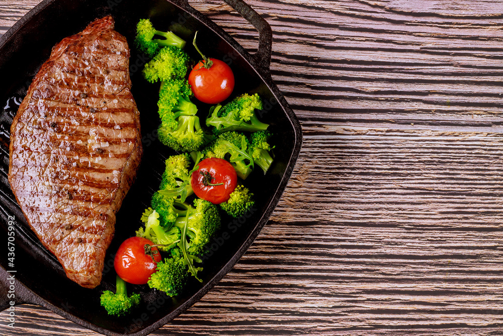 Wall mural Grilled rare beef steak with broccoli and tomato on grill pan.