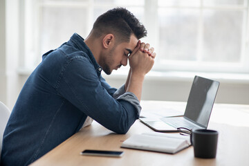 Depressed arab man sitting in front of laptop, office interior