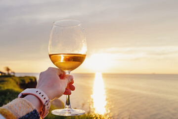 Woman hand holding a glass of rose wine at sunset