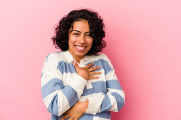 Young curly latin woman isolated on pink background laughs happily and has fun keeping hands on...