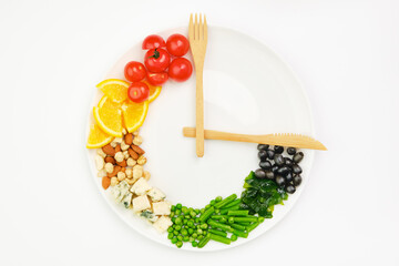 Colorful food and cutlery arranged in the form of a clock on a plate. Intermittent fasting, diet,...