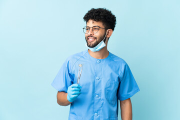 Moroccan dentist man holding tools isolated on blue background looking side