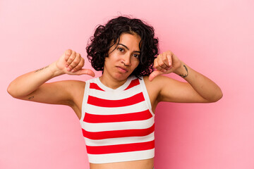 Young curly latin woman isolated on pink background showing a dislike gesture, thumbs down. Disagreement concept.