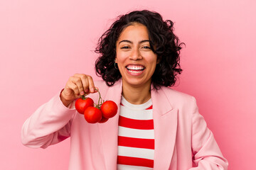 Young latin woman holding tomatoes isolated on pink background