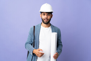 Young architect Moroccan man with helmet and holding blueprints over isolated background with...