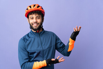 Young Moroccan cyclist man isolated on purple background extending hands to the side for inviting to come - obrazy, fototapety, plakaty
