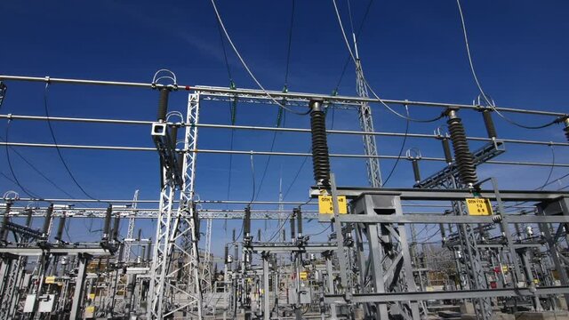 Motion past glass insulators on supports and cable bus pipes in switchyard of contemporary substation under clear blue sky