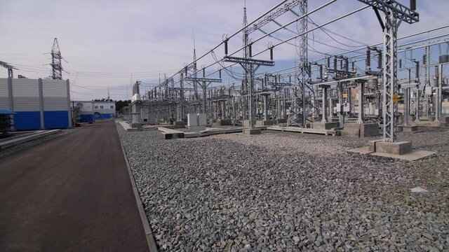 Glass insulators stack on supports with cable bus pipes empty road and building at switchyard of substation under blue sky