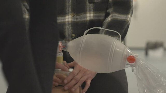 Person Holding A Bag Valve Mask On A Dummy's Mouth While Another Is Doing CPR