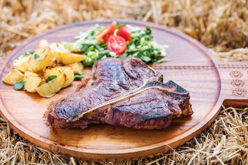 Dry aged steak on a wooden board with potatoes and cherry tomato and lettuce 