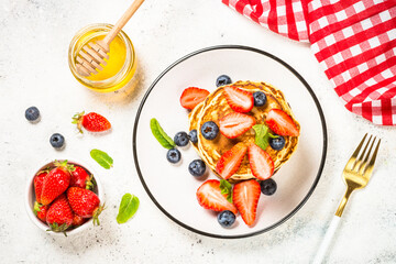 Pancakes with fresh berries and honey at white table. Healthy breakfast or dessert. Top view with copy space.