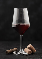 Glass of red wine with corks and vintage corkscrew on dark.