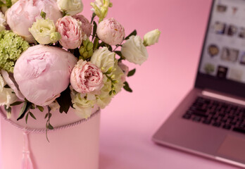 bouquet of flowers in a box close-up, against the background of an open laptop. Selective focus. Hydrangea, roses and peonies on a pink background. home delivery concept, buying flowers online. 