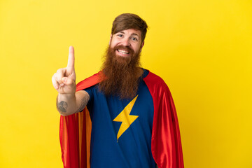 Redhead Super Hero man isolated on yellow background showing and lifting a finger