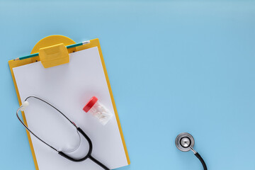 Clear pill bottle, stethoscope and a notepad on a blue background.