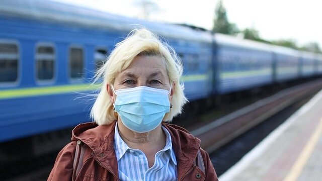 Close up senior woman with medicine mask on the face at public train station platform during coronavirus Covid-19 pandemic. Travel by train