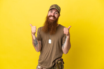 Redhead Military man with dog tag isolated on yellow background with thumbs up gesture and smiling