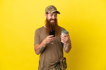 Redhead Military man with dog tag isolated on yellow background holding coffee to take away and a...