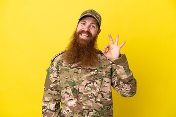 Military Redhead man over isolated on yellow background showing ok sign with fingers