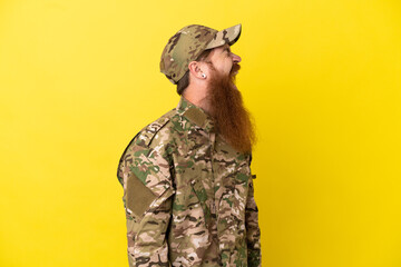 Military Redhead man over isolated on yellow background laughing in lateral position