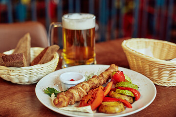 grilled chicken with  vegetables tomato carrot and zucchini served with hot sauce on a big plate and cold  beer eaten at the restaraurant