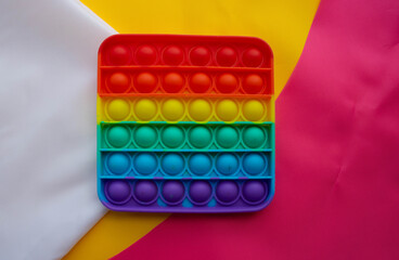 The rainbow toy lies against a background of pink and yellow white fabric. Blue and Orange Funny Interactive Anti-Stress Silicone Toys. Pop it