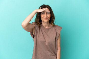 Middle aged caucasian woman isolated on blue background looking far away with hand to look something